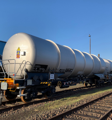 Grauer Kesselwagen auf Gleis unter blauem Himmel